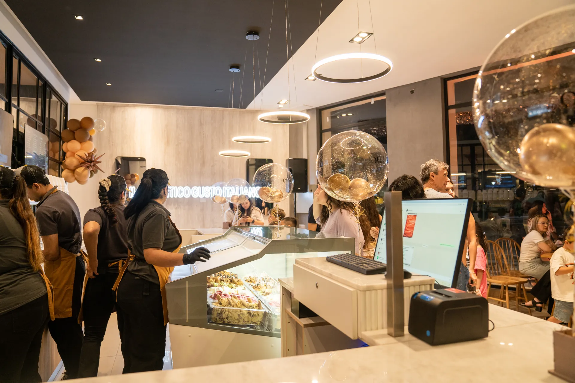 Salón de il Biondo colmado de gente, con la vitrina de helados y el cartel de neón